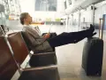 Kobieta z walizką siedzi na lotnisku, trzymając dokumenty.