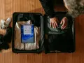 Osoba pakuje walizkę, w której widać ubrania, buty i tablet z ekranem Windows.