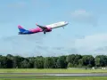 Samolot Wizz Air wznosi się na tle błękitnego nieba z chmurami.