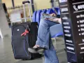 Czarny walizka z niebieskimi akcentami i czerwoną wstążką, obok siedzącej osoby w dżinsach.