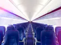 Wnętrze samolotu Wizz Air z rzędami niebieskich foteli i fioletowym oświetleniem.