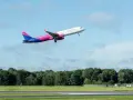Samolot Wizz Air wznoszący się na tle błękitnego nieba z chmurami.