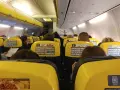 Widok z wnętrza samolotu Ryanair z żółtymi siedzeniami i pasażerami.