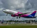 Samolot Wizz Air z różowymi silnikami startuje na tle chmur.