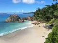 Plaża na Seszelach z turkusową wodą, palmami i formacjami skalnymi.