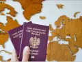 Dłoń trzyma dwa polskie paszporty na tle drewnianej mapy Europy.