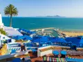 Widok na zatokę z łodziami, plażę i kawiarnię z niebieskimi parasolami.