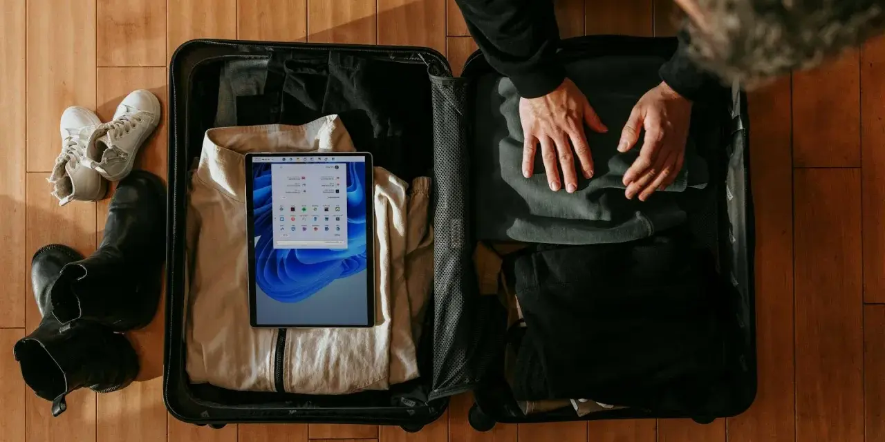 Osoba pakuje walizkę, w której widać ubrania, buty i tablet z ekranem Windows.