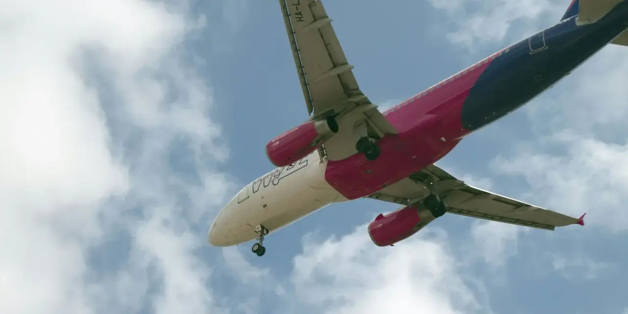 Samolot Wizzair w locie, widok od dołu, na tle błękitnego nieba z chmurami.