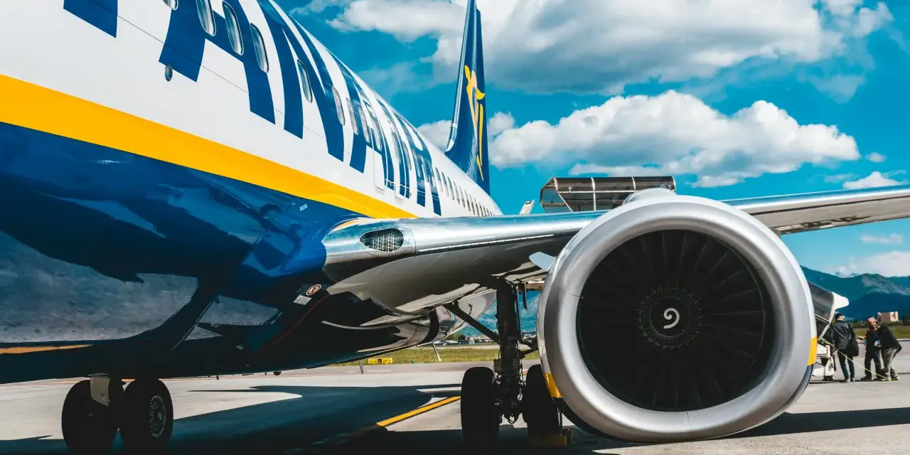 Fragment samolotu Ryanair z widocznym silnikiem i podwoziem na tle nieba.