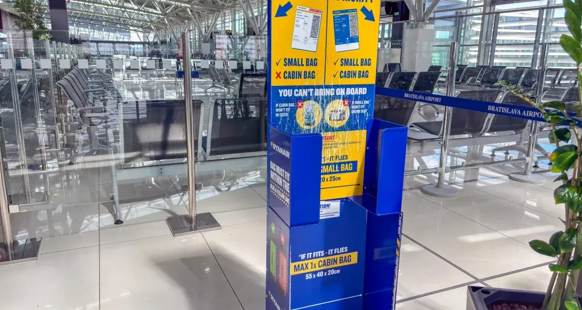 Niebieski stojak Ryanair z informacjami o bagażu w poczekalni lotniskowej.