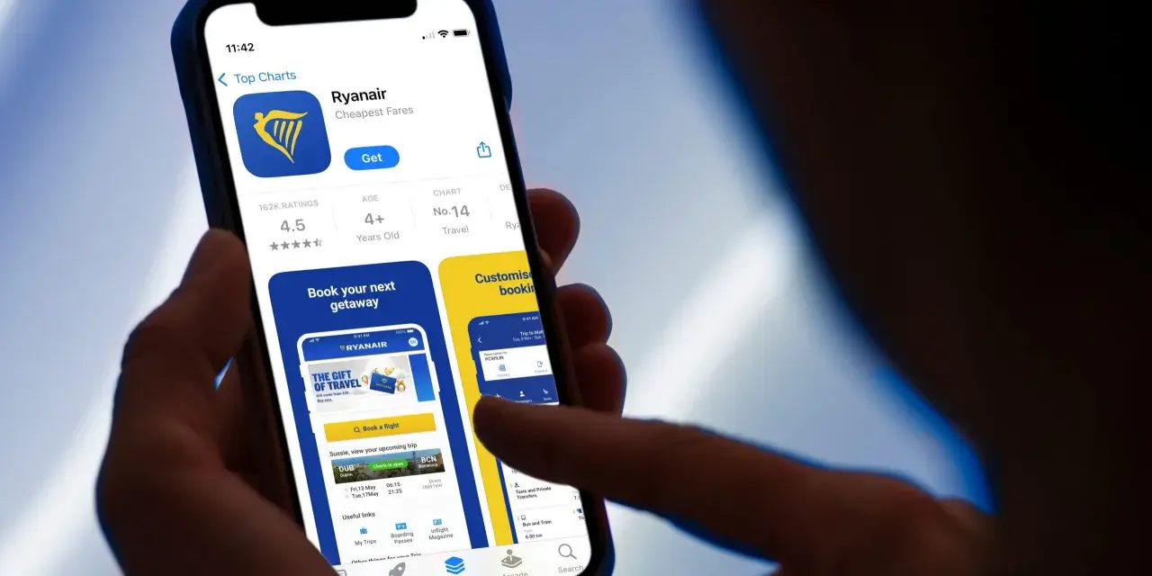 Dłoń trzyma smartfon z otwartą aplikacją Ryanair, widoczny ekran z logo i opcjami.
