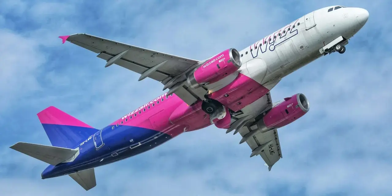 Samolot Wizz Air z różowymi silnikami i ogonem wznosi się na tle błękitnego nieba.