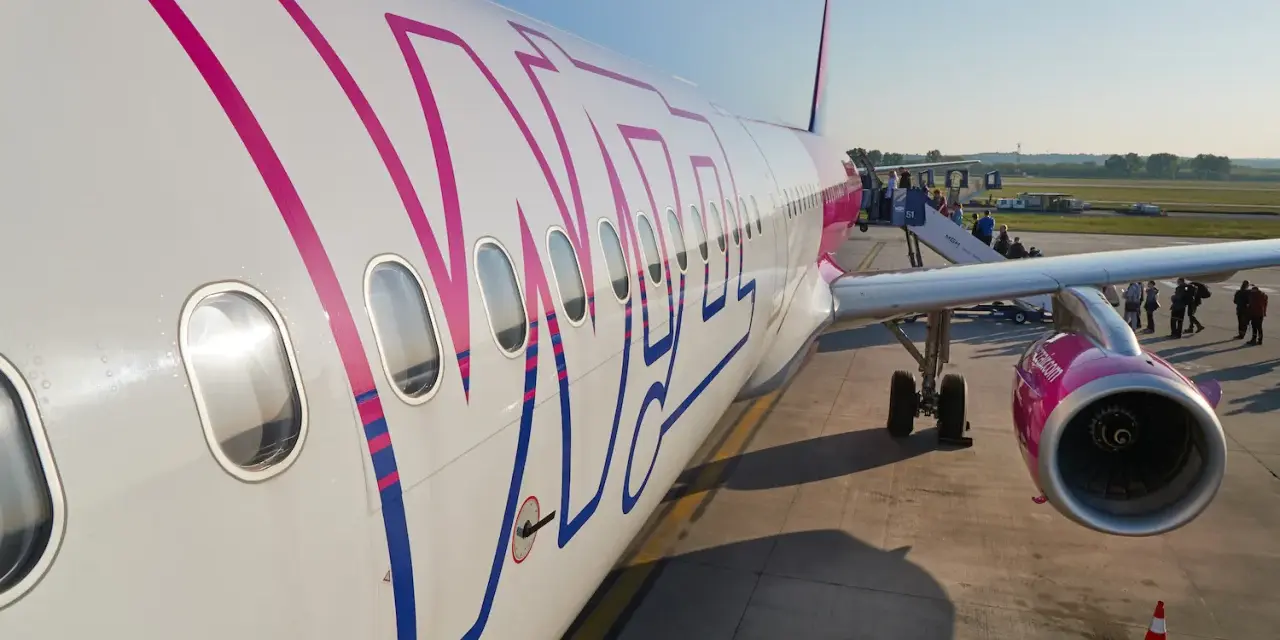 Samolot Wizz Air z pasażerami wsiadającymi po schodkach na lotnisku.