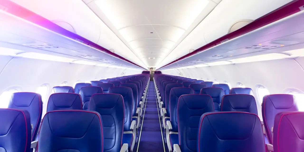 Wnętrze samolotu Wizz Air z rzędami niebieskich foteli i fioletowym oświetleniem.