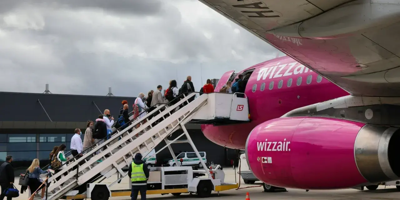 Pasażerowie wsiadają po schodkach do różowego samolotu Wizz Air.