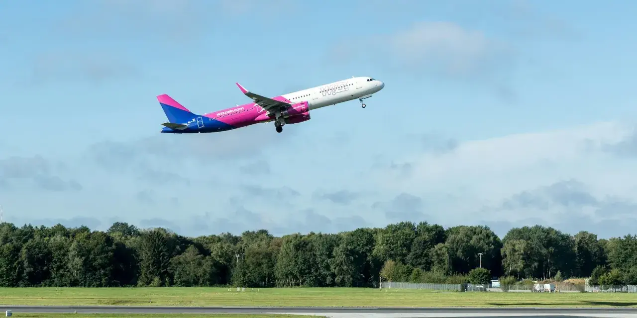 Samolot Wizz Air wznoszący się na tle błękitnego nieba z chmurami.