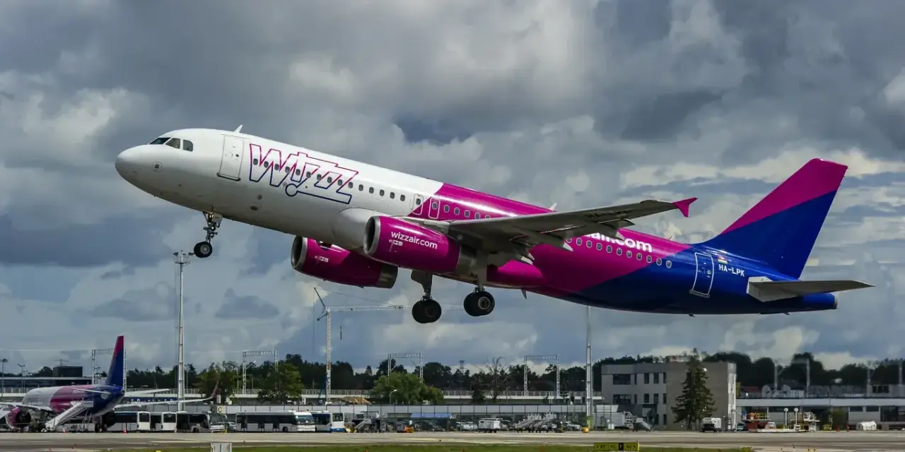 Samolot Wizz Air z różowymi silnikami startuje na tle chmur.