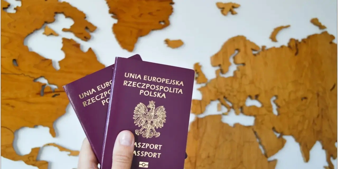 Dłoń trzyma dwa polskie paszporty na tle drewnianej mapy Europy.