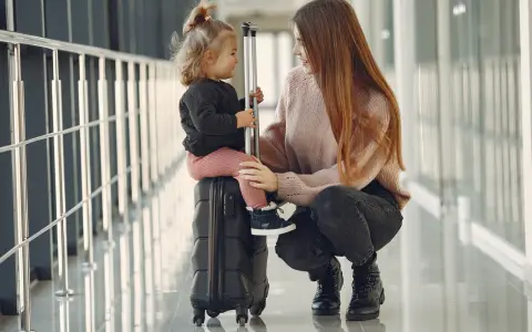 Kobieta kuca obok walizki, na której siedzi dziecko.