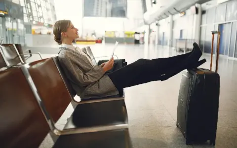 Kobieta z walizką siedzi na lotnisku, trzymając dokumenty.