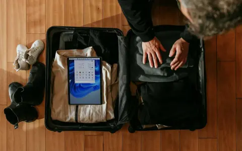 Osoba pakuje walizkę, w której widać ubrania, buty i tablet z ekranem Windows.