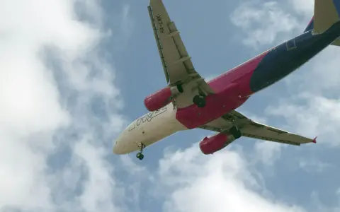 Samolot Wizzair w locie, widok od dołu, na tle błękitnego nieba z chmurami.