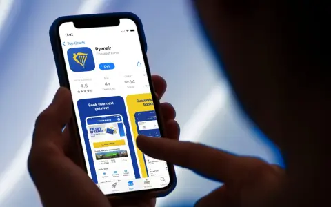 Dłoń trzyma smartfon z otwartą aplikacją Ryanair, widoczny ekran z logo i opcjami.