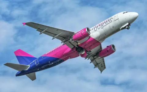 Samolot Wizz Air z różowymi silnikami i ogonem wznosi się na tle błękitnego nieba.