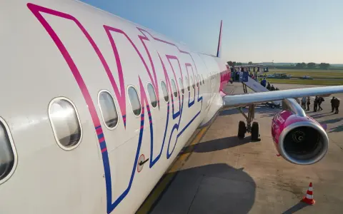 Samolot Wizz Air z pasażerami wsiadającymi po schodkach na lotnisku.