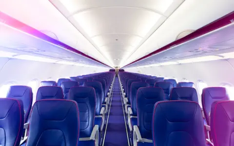 Wnętrze samolotu Wizz Air z rzędami niebieskich foteli i fioletowym oświetleniem.