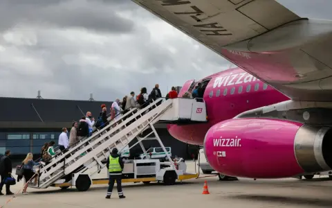 Pasażerowie wsiadają po schodkach do różowego samolotu Wizz Air.