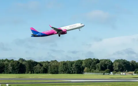 Samolot Wizz Air wznoszący się na tle błękitnego nieba z chmurami.