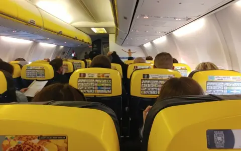 Widok z wnętrza samolotu Ryanair z żółtymi siedzeniami i pasażerami.