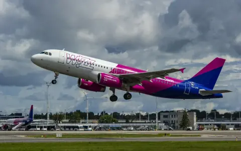 Samolot Wizz Air z różowymi silnikami startuje na tle chmur.