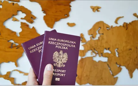 Dłoń trzyma dwa polskie paszporty na tle drewnianej mapy Europy.