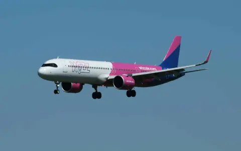 Samolot Wizz Air z wysuniętym podwoziem na tle błękitnego nieba.