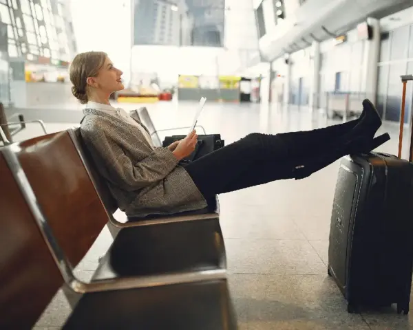 Kobieta z walizką siedzi na lotnisku, trzymając dokumenty.