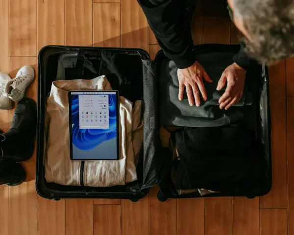 Osoba pakuje walizkę, w której widać ubrania, buty i tablet z ekranem Windows.