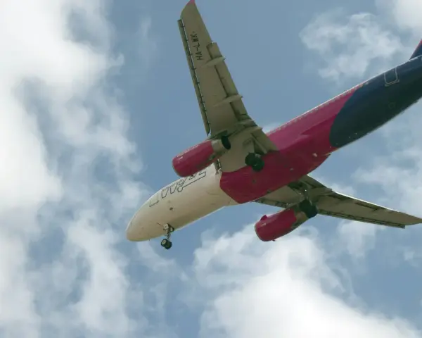 Samolot Wizzair w locie, widok od dołu, na tle błękitnego nieba z chmurami.