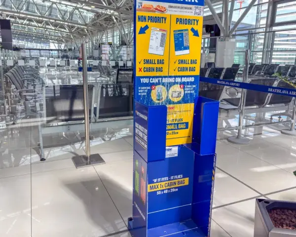 Niebieski stojak Ryanair z informacjami o bagażu w poczekalni lotniskowej.