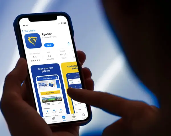 Dłoń trzyma smartfon z otwartą aplikacją Ryanair, widoczny ekran z logo i opcjami.