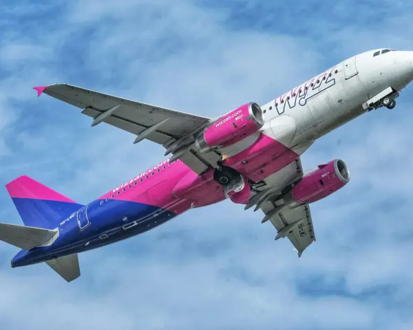Samolot Wizz Air z różowymi silnikami i ogonem wznosi się na tle błękitnego nieba.