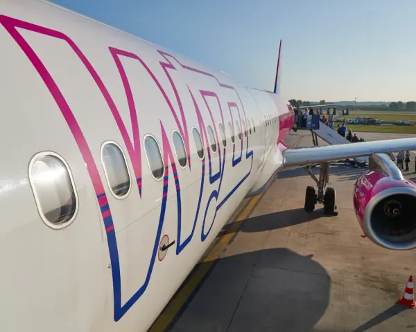 Samolot Wizz Air z pasażerami wsiadającymi po schodkach na lotnisku.