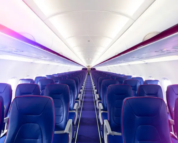Wnętrze samolotu Wizz Air z rzędami niebieskich foteli i fioletowym oświetleniem.