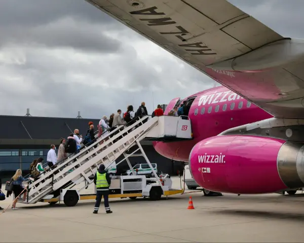 Pasażerowie wsiadają po schodkach do różowego samolotu Wizz Air.