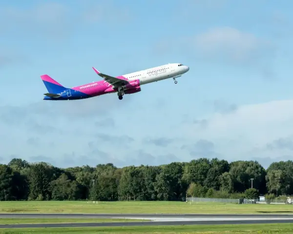 Samolot Wizz Air wznoszący się na tle błękitnego nieba z chmurami.