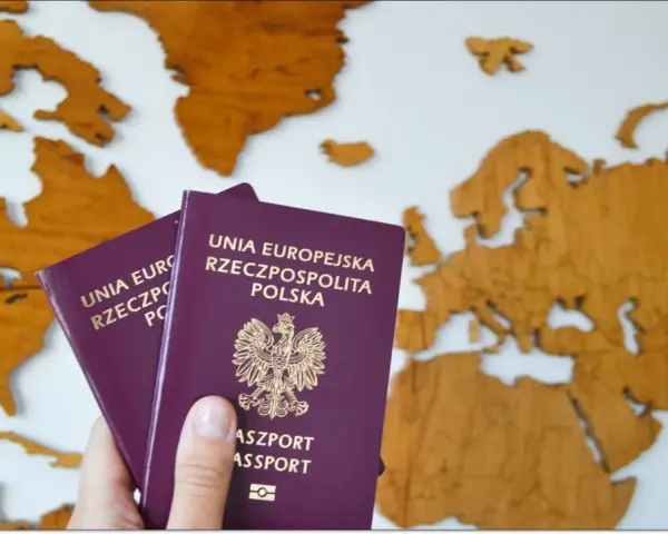 Dłoń trzyma dwa polskie paszporty na tle drewnianej mapy Europy.