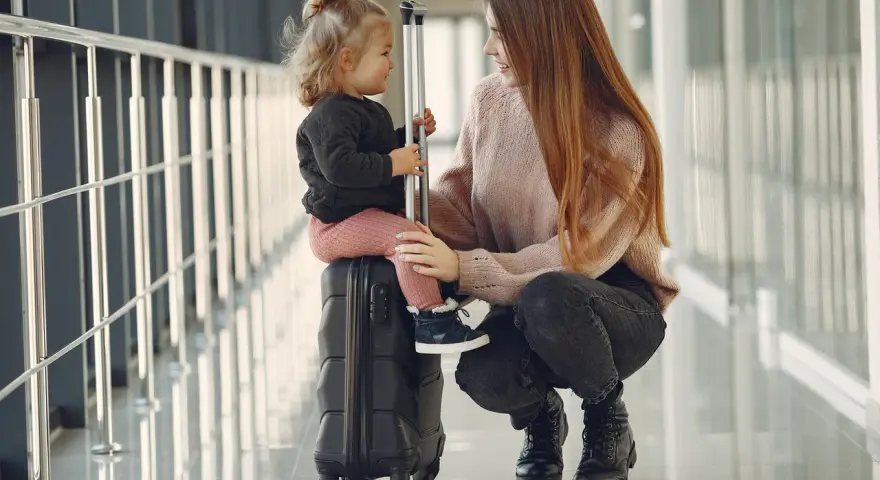 Kobieta kuca obok walizki, na której siedzi dziecko.