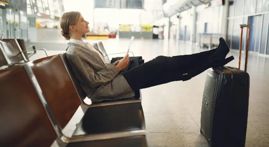 Kobieta z walizką siedzi na lotnisku, trzymając dokumenty.
